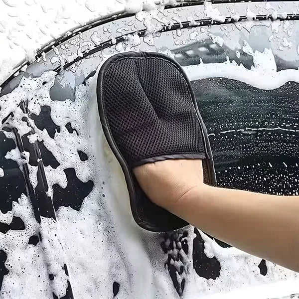 Person cleaning a car window with a black mitt covered in soap suds.