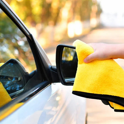 Person cleaning a car mirror with a yellow microfiber cloth.