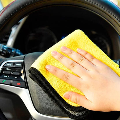 Hand holding a yellow microfiber cloth over a car's steering wheel