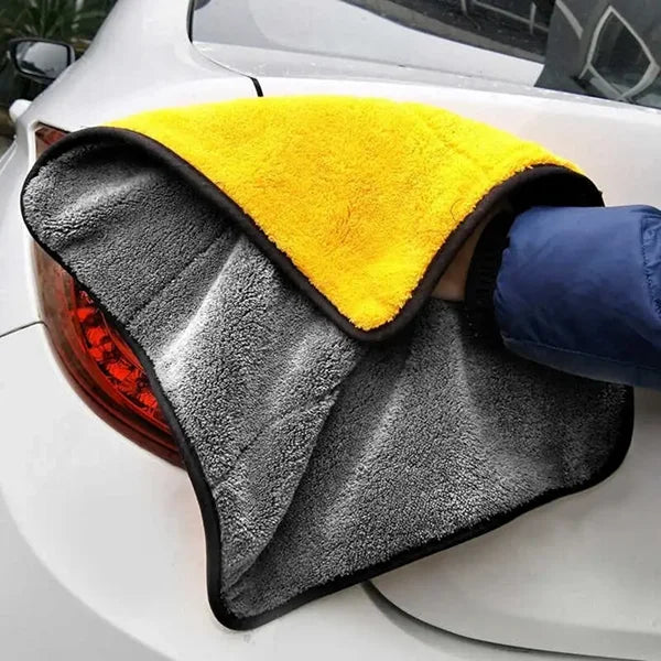 Person using a gray and yellow microfiber towel on a car's taillight.